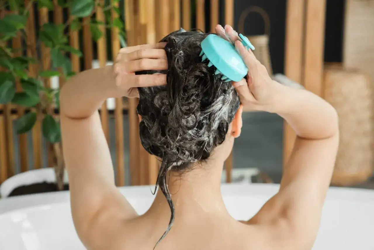 Persona lava i capelli con uno spazzolino azzurro. Ricorda, lavare i capelli tutti i giorni fa male.
