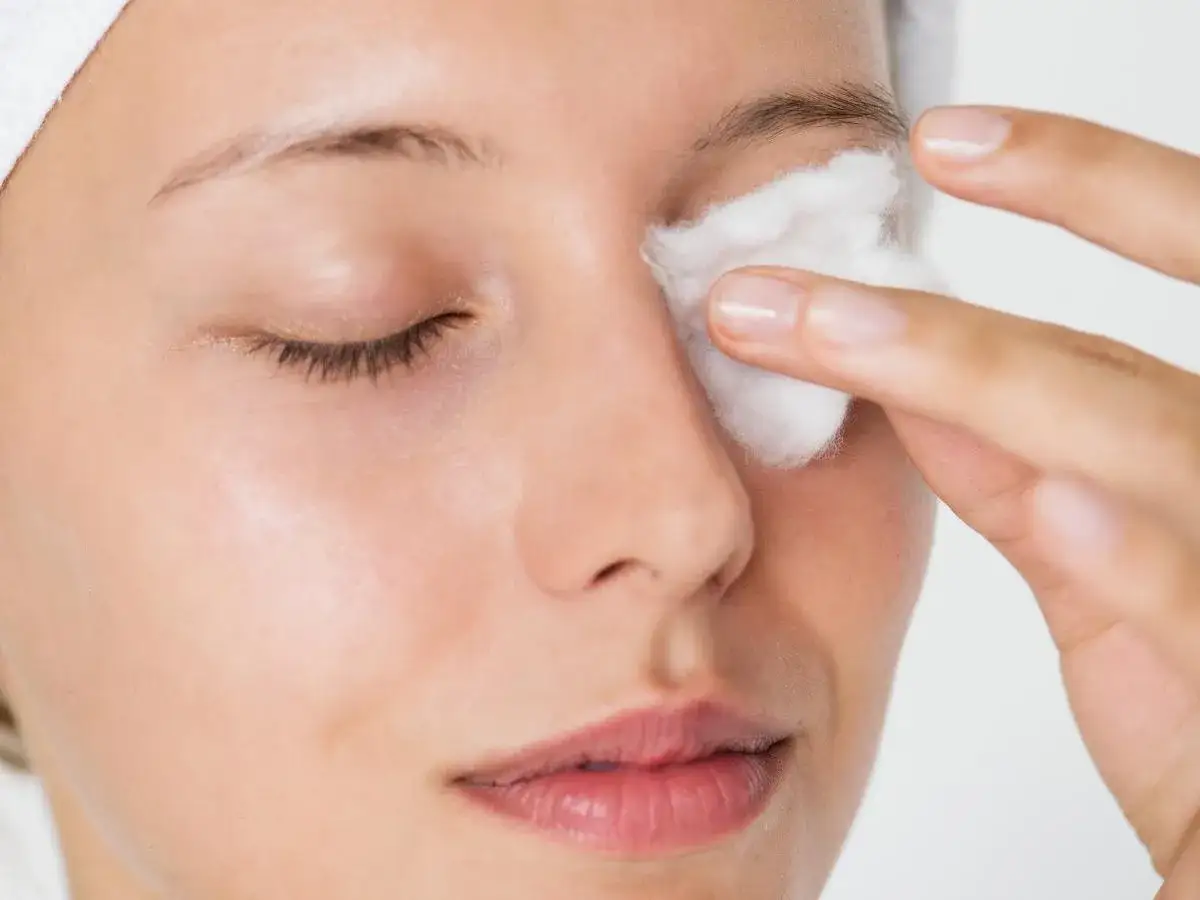 Donna rimuove il trucco con un dischetto imbevuto di latte detergente o acqua micellare.
