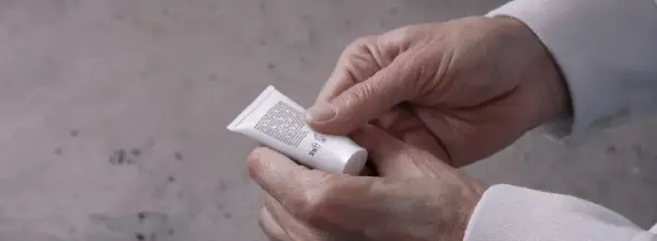 Mani che stringono un tubetto di crema, forse un trattamento iodase anticellulite tiroide, leggendo attentamente gli ingredienti.