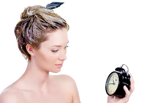 Donna con capelli trattati con maschera, osserva un orologio. Impara come si usa la maschera per capelli per un trattamento efficace.