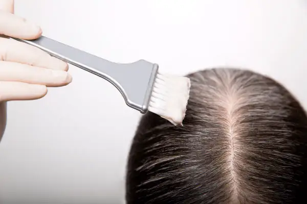 Guanto e pennello applicano tinta sui capelli scuri, mostrando come fare la tinta in casa per un cambio look.