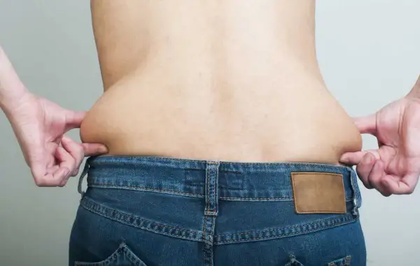 Mani che stringono i fianchi larghi di un uomo, evidenziando accumuli di grasso sopra i jeans.