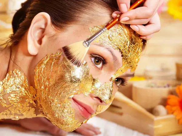 Una donna riceve un trattamento di bellezza con una maschera viso oro, scoprendo i suoi benefici rigeneranti.