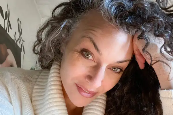 Donna con capelli ricci e grigi, che riflette sulle cause della ricrescita capelli bianchi troppo veloce.