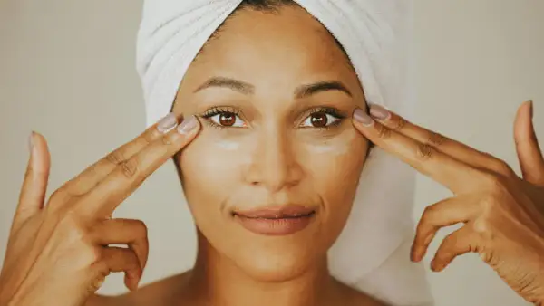 Donna con turbante applica crema contorno occhi, mostrando la differenza tra unguento e crema per la cura della pelle.