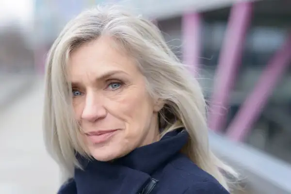 Donna con capelli biondo cenere, un sorriso discreto e occhi azzurri. Nonostante i capelli bianchi, il suo look è curato, quasi a voler camuffare capelli bianchi con un'eleganza naturale.