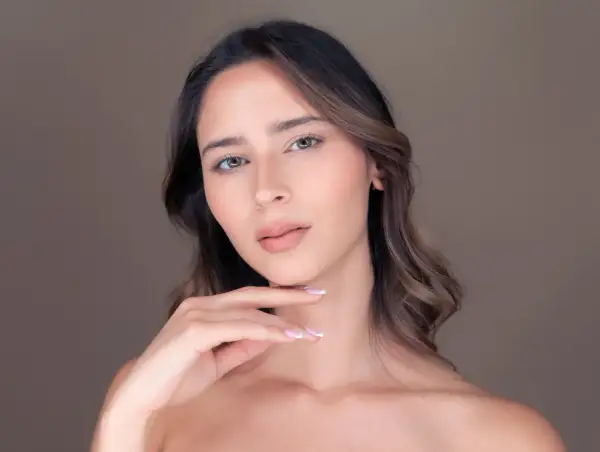 Viso di donna con pelle luminosa, effetto di retinolo e acido ialuronico. Mano sfiora il mento.