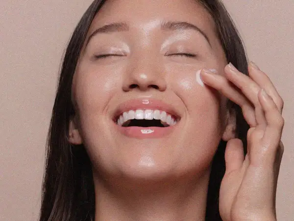 Viso radioso di una donna che applica una crema, un gesto che ricorda cos'è lo scrub per una pelle luminosa e liscia.