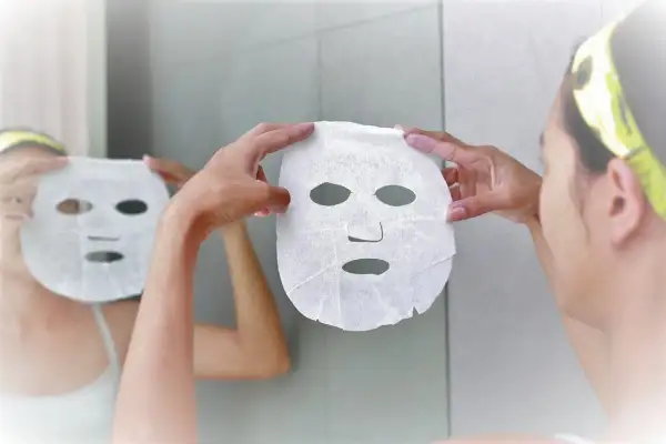 Una donna si prepara per una maschera viso, riflettendosi allo specchio. Scopri quando farla per una pelle radiosa.