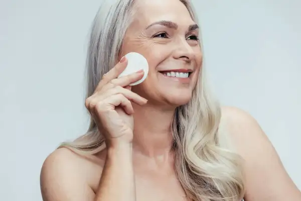 Donna sorridente con cotone per la pulizia del viso, mostrando la differenza tra latte detergente e detergente viso.