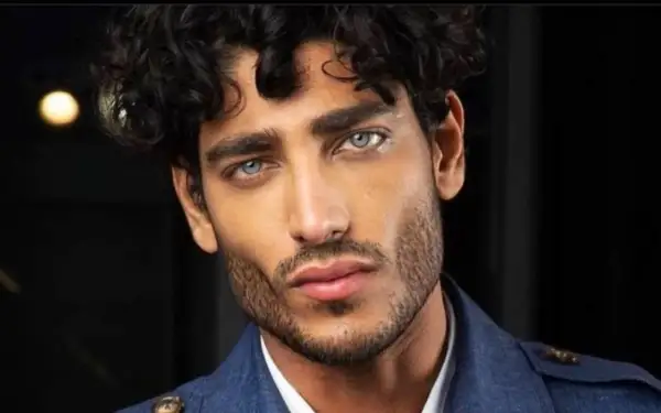 Uomo con capelli mossi scuri e occhi azzurri penetranti, un look che ispira su come farsi i capelli mossi uomo.