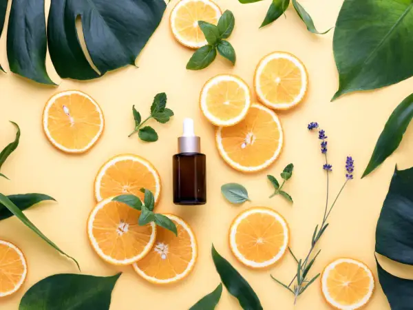Siero viso con niacinamide e vitamina c, circondato da fette d'arancia, foglie verdi e lavanda.