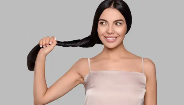 Una donna sorride mentre tiene una ciocca dei suoi lunghi capelli neri. Sembra che si chieda: "henne cos'è?