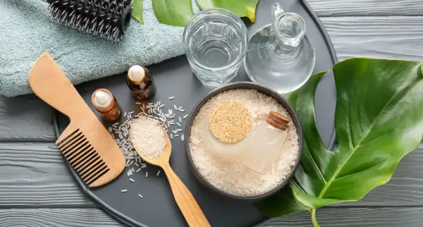 Ingredienti naturali per la cura dei capelli: riso, acqua, oli essenziali, pettine e spazzola. L'acqua di riso capelli è un segreto di bellezza.