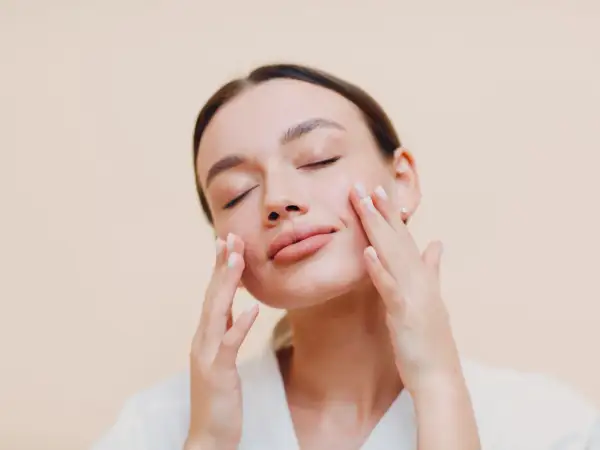 Donna con occhi chiusi applica delicatamente una crema sebo regolatrice sul viso, godendosi un momento di cura della pelle.