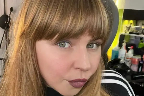 Ragazza con capelli castani e una frangia che incornicia il viso. Sguardo intenso e labbra color prugna.