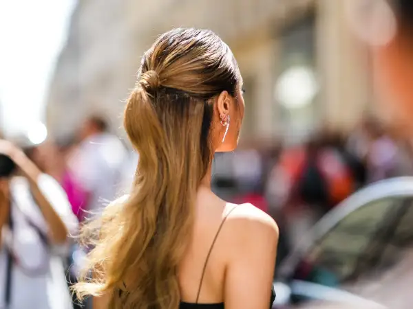 Capelli lunghi e ondulati, di un caldo biondo miele, raccolti in una coda bassa. Orecchini luminosi completano il look.