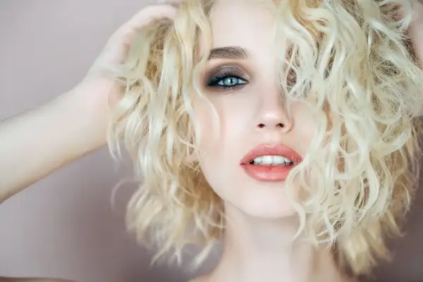 Capelli biondi e ricci, luminosi come la camomilla, incorniciano un volto con occhi azzurri e labbra sensuali.